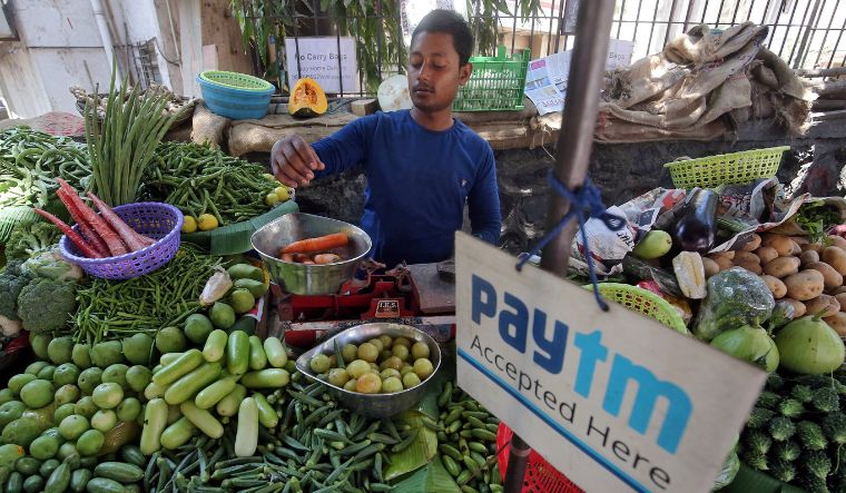 A vendor weighs vegetable next to an advertisement of Paytm hanging amidst his vegetables at a roadside market in Mumbai